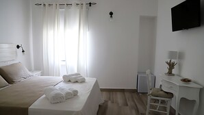 Habitación de hotel con cama, escritorio, silla, televisión y una pequeña mesa con un objeto decorativo.