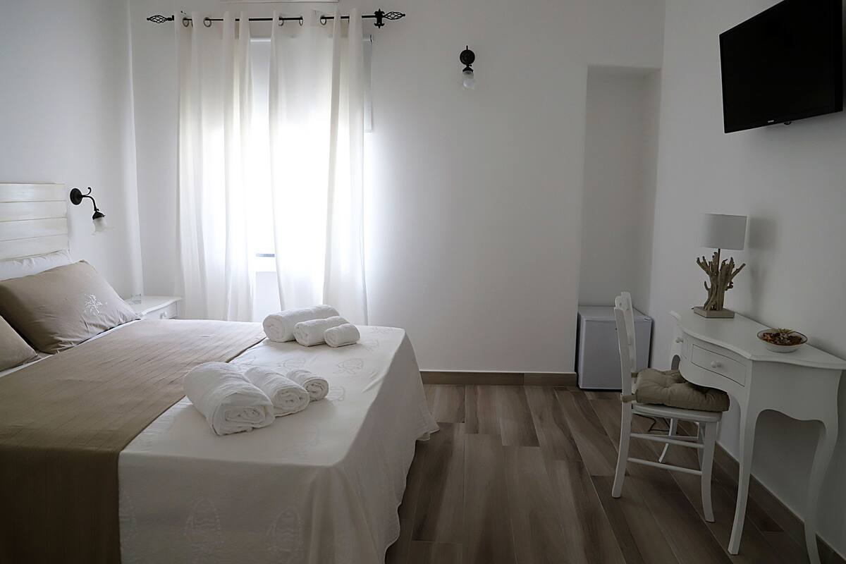 Une chambre d’hôtel comprenant un lit, un bureau, une chaise, une télévision et une petite table agrémentée d’un objet décoratif.