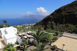 Une terrasse sur le toit avec des sièges extérieurs, un palmier et une vue sur la mer et les montagnes lointaines.