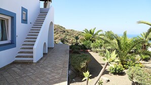 Un edificio blanco con una escalera que conduce a un balcón con vistas a un jardín de palmeras y al mar.
