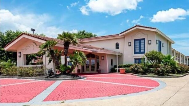 Un edificio de dos pisos con techo de tejas rojas, un porche cubierto y un área ajardinada con alfombra roja.