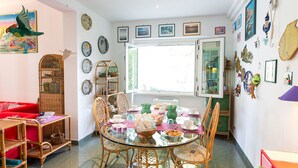 A cozy living room with a red sofa, a glass dining table, wicker chairs, and a variety of decorative plates on the walls. - B&B Amoredimare (Polignano a Mare)