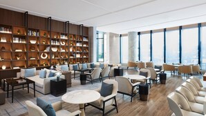Un moderno vestíbulo de hotel con una amplia estantería, asientos cómodos y grandes ventanales que ofrecen vistas a la ciudad.