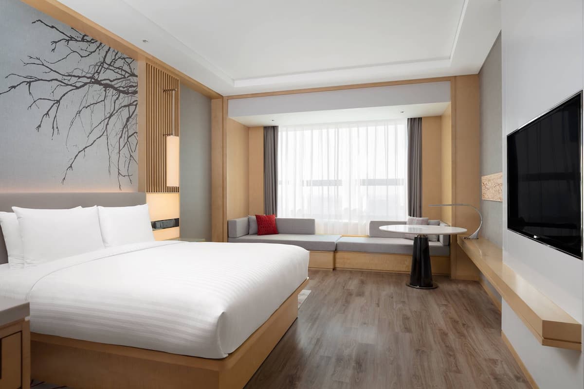A modern hotel room with a large bed, a seating area with a table, and a TV mounted on the wall.