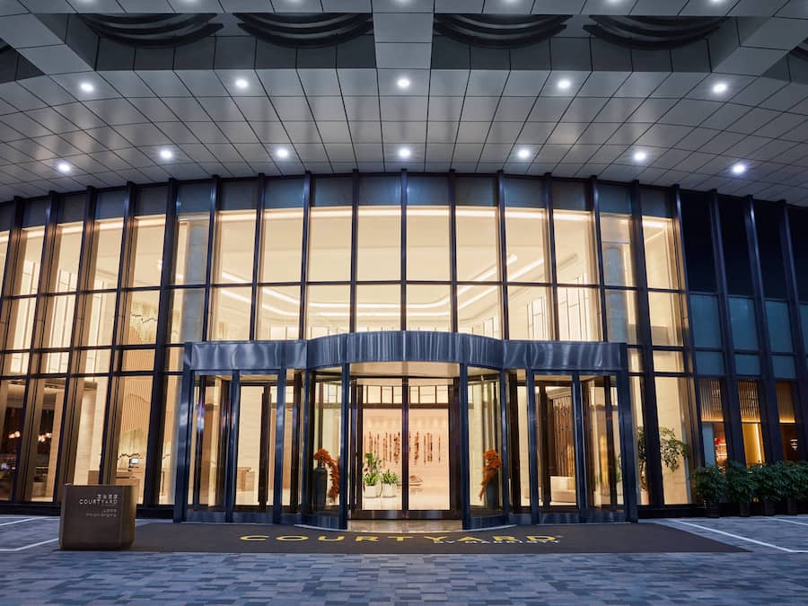 Una entrada de hotel moderna con fachada curva, grandes ventanales y un espacio de recepción acogedor.
