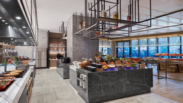 Una cocina moderna con encimeras de mármol, una zona de bufé con diversas opciones de comida y un amplio ventanal con vistas al exterior.