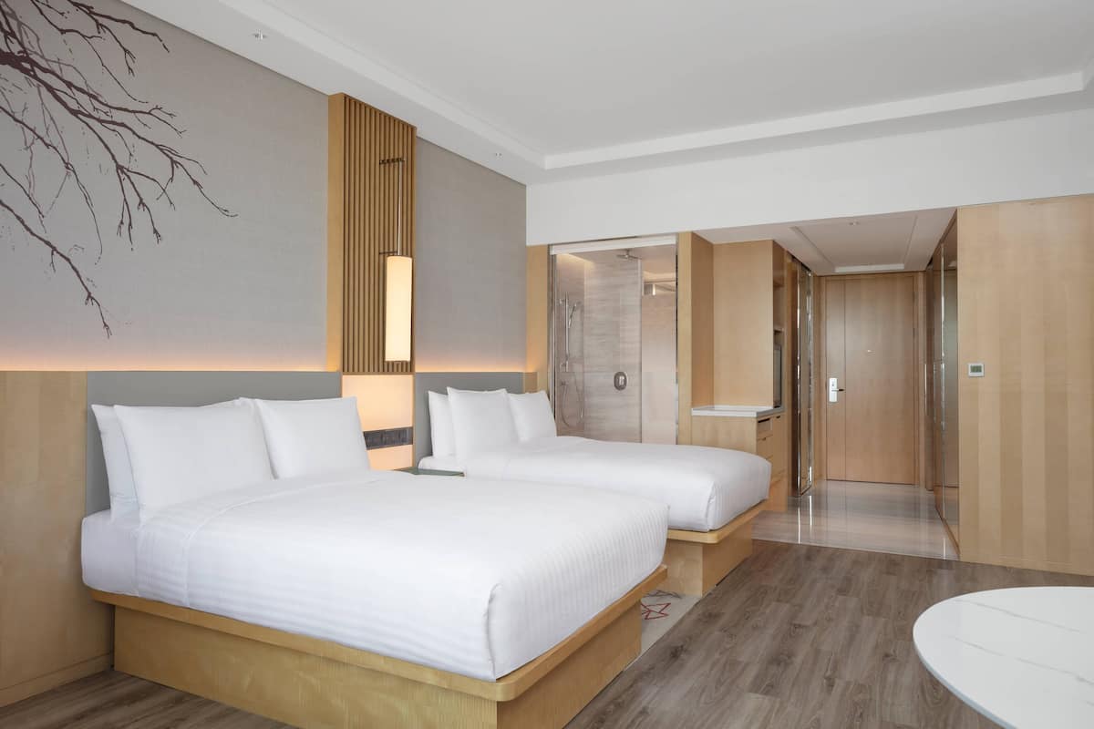 A hotel room with two beds, a large wall art piece, a modern bathroom, and a wooden floor.