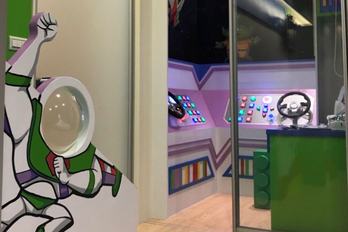 A room with a large window, a control panel with colorful lights, and a wall with a character design.