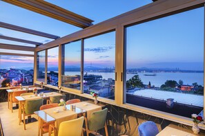 Un restaurant doté de grandes fenêtres donnant sur un paysage urbain et sur une étendue d’eau.