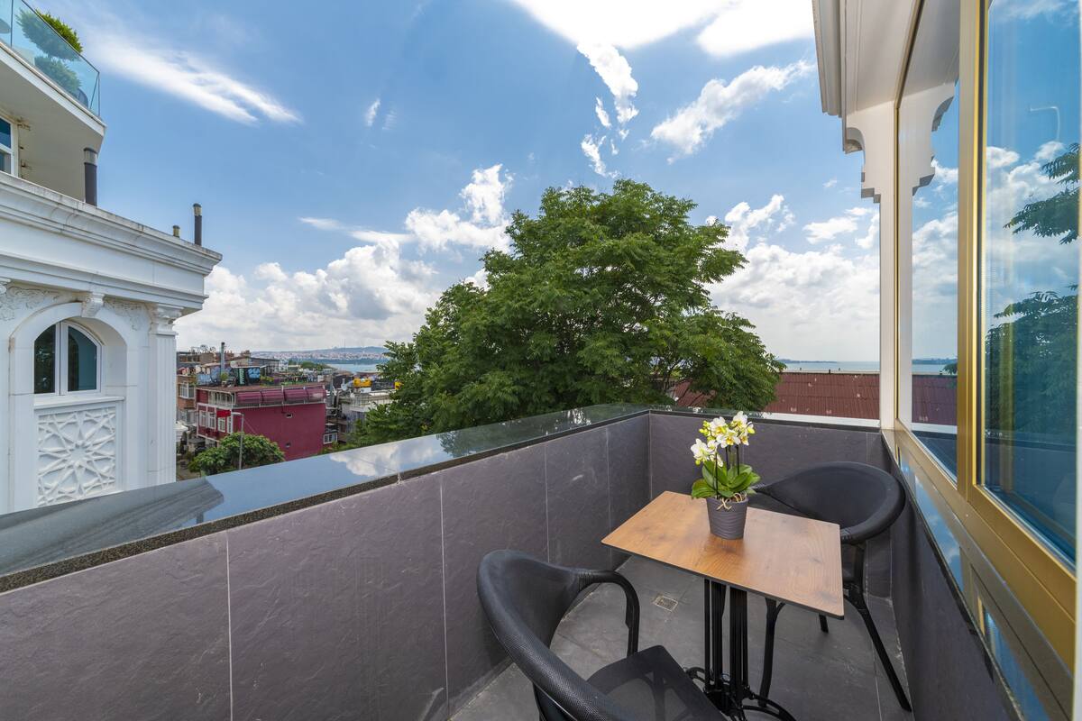 A balcony with a table and chairs, a potted plant, and a view of the cityscape.
