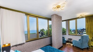 A modern hotel room with a large bed, a seating area with a chair and a small table, and large windows offering a view of the outdoors. - Eastanbul Suites (Istanbul)