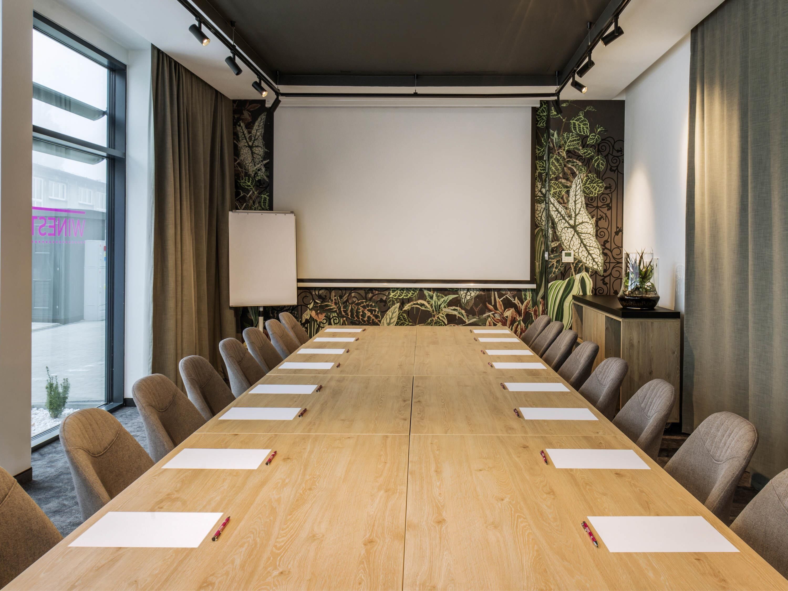 Ein Konferenzraum mit langem Tisch, Stühlen, einer Projektionsleinwand und einer Wandverzierung.