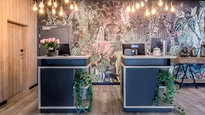 Un comptoir d’accueil orné d’une fresque florale, deux postes informatiques et des lampes suspendues.