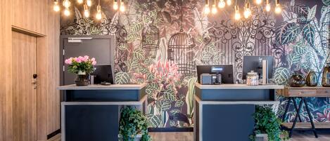 A reception desk with a floral mural, two computer stations, and hanging light bulbs.