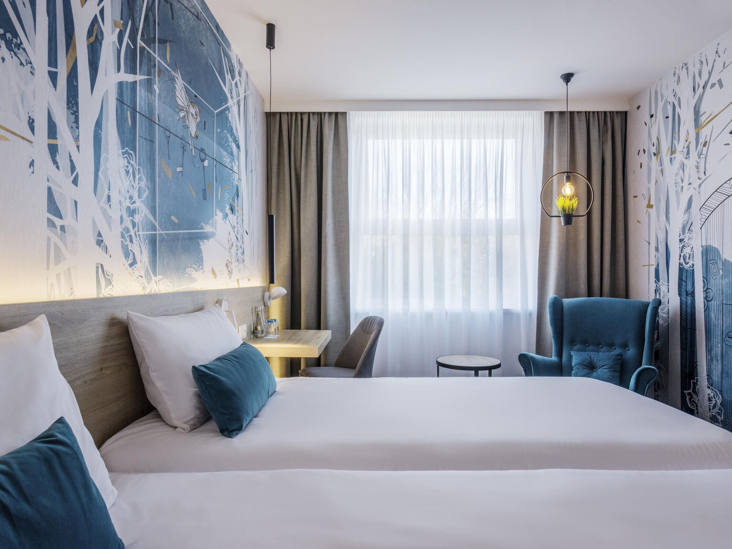 A hotel room with a large bed, a desk, a chair, and a window with curtains.
