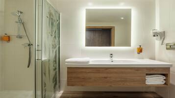 A modern bathroom with a glass shower enclosure, a wooden vanity, a large mirror, and a built-in towel rack.