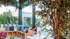 Un enfant est assis à une table, devant des livres, un jouet en bois et une plante en pot.
