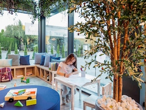 Een kind aan een tafel met boeken, een houten speeltje en een bloempot.
