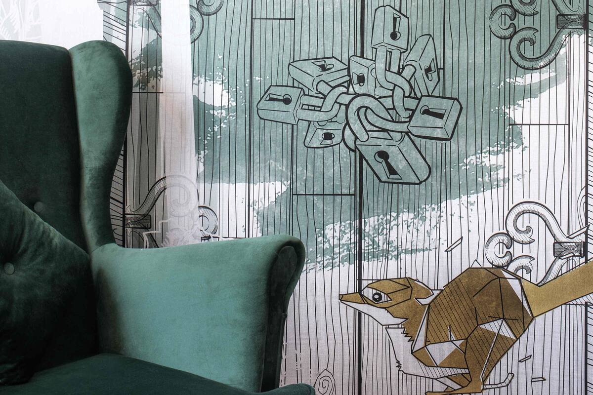 Ein Zimmer mit einem grünen Sessel, einem gemusterten Vorhang und einer Wand mit einer geometrischen Vogelillustration.