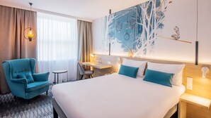 Une chambre d’hôtel avec un grand lit, un bureau, une chaise et un mur orné d’un motif géométrique.