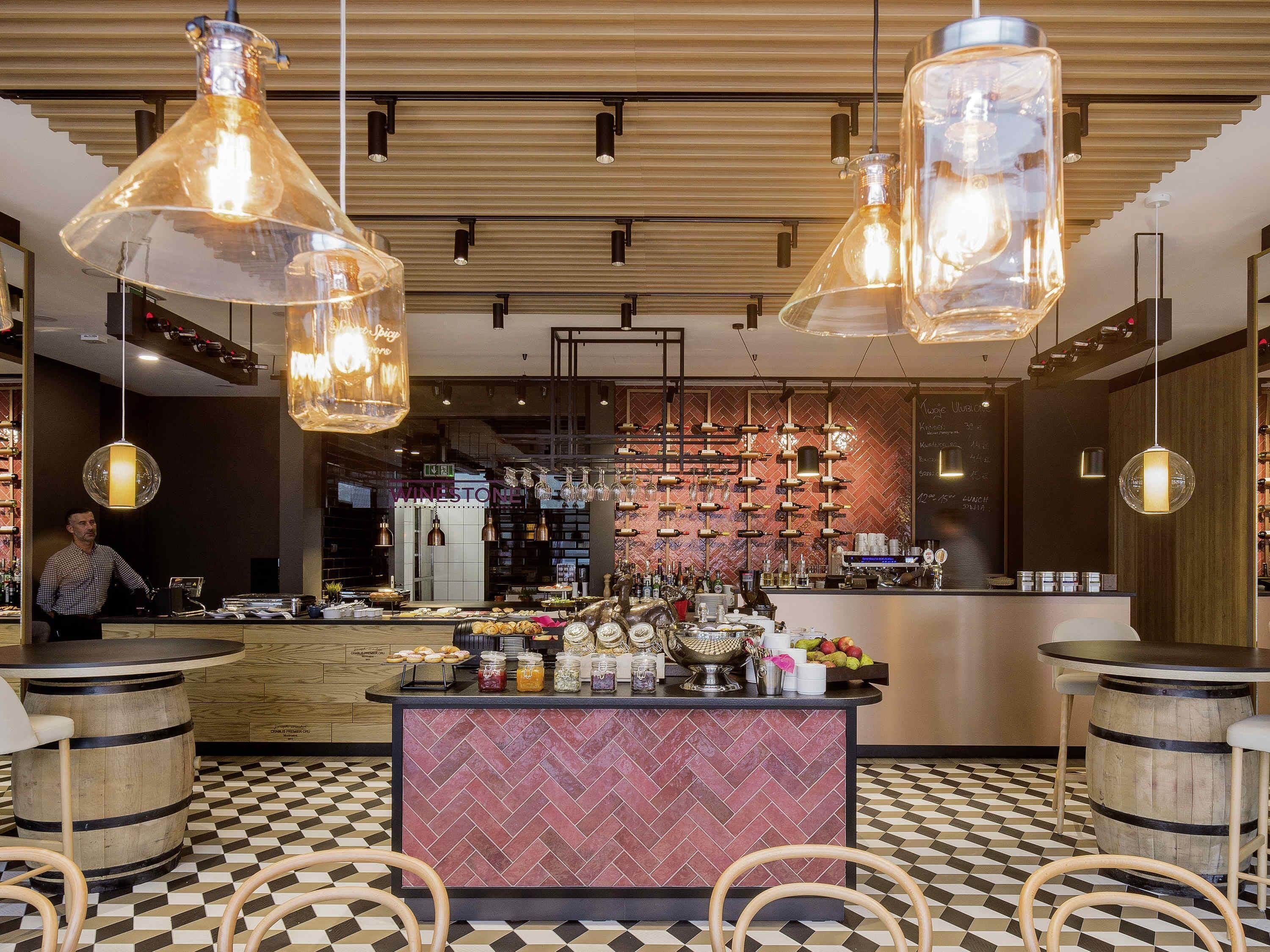 A bar area with a herringbone patterned floor, wooden barrels, and a central bar counter with various items displayed.