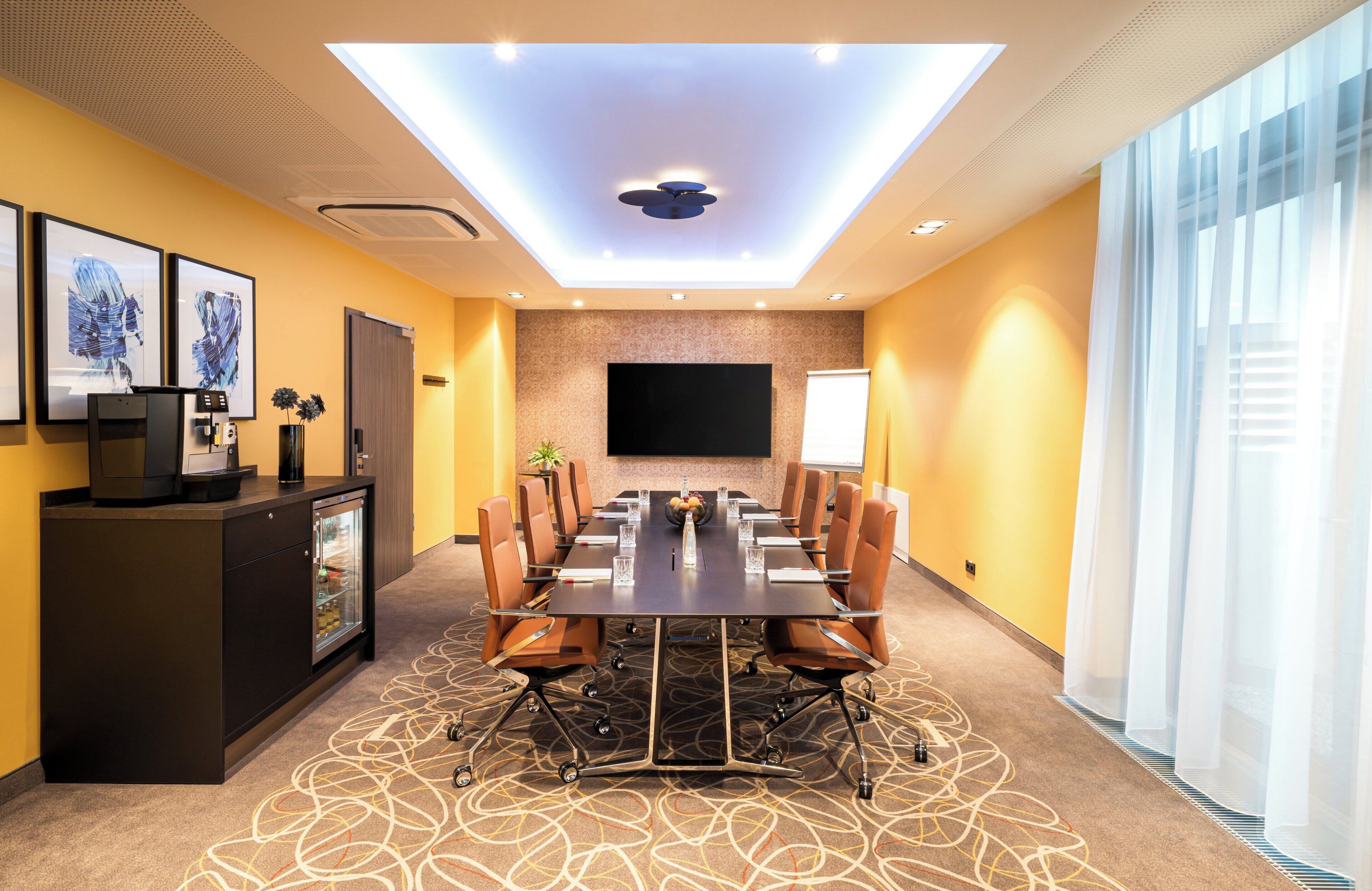 A conference room with a long table, chairs, a TV screen, and a reception desk.