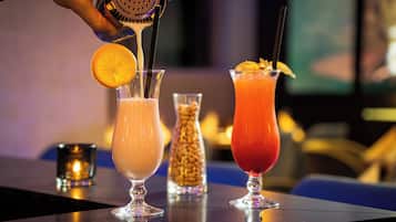 Three cocktails on a bar counter with a hand pouring a drink into one of them.