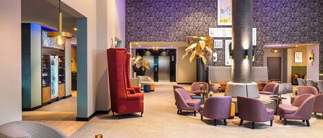 A lobby with a modern design, featuring a reception desk, seating area with armchairs and sofas, and a large decorative plant.