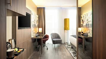 Een hotelkamer met een flatscreen televisie, een bureau met lamp, een stoel, een bed en een groot raam met gordijnen.
