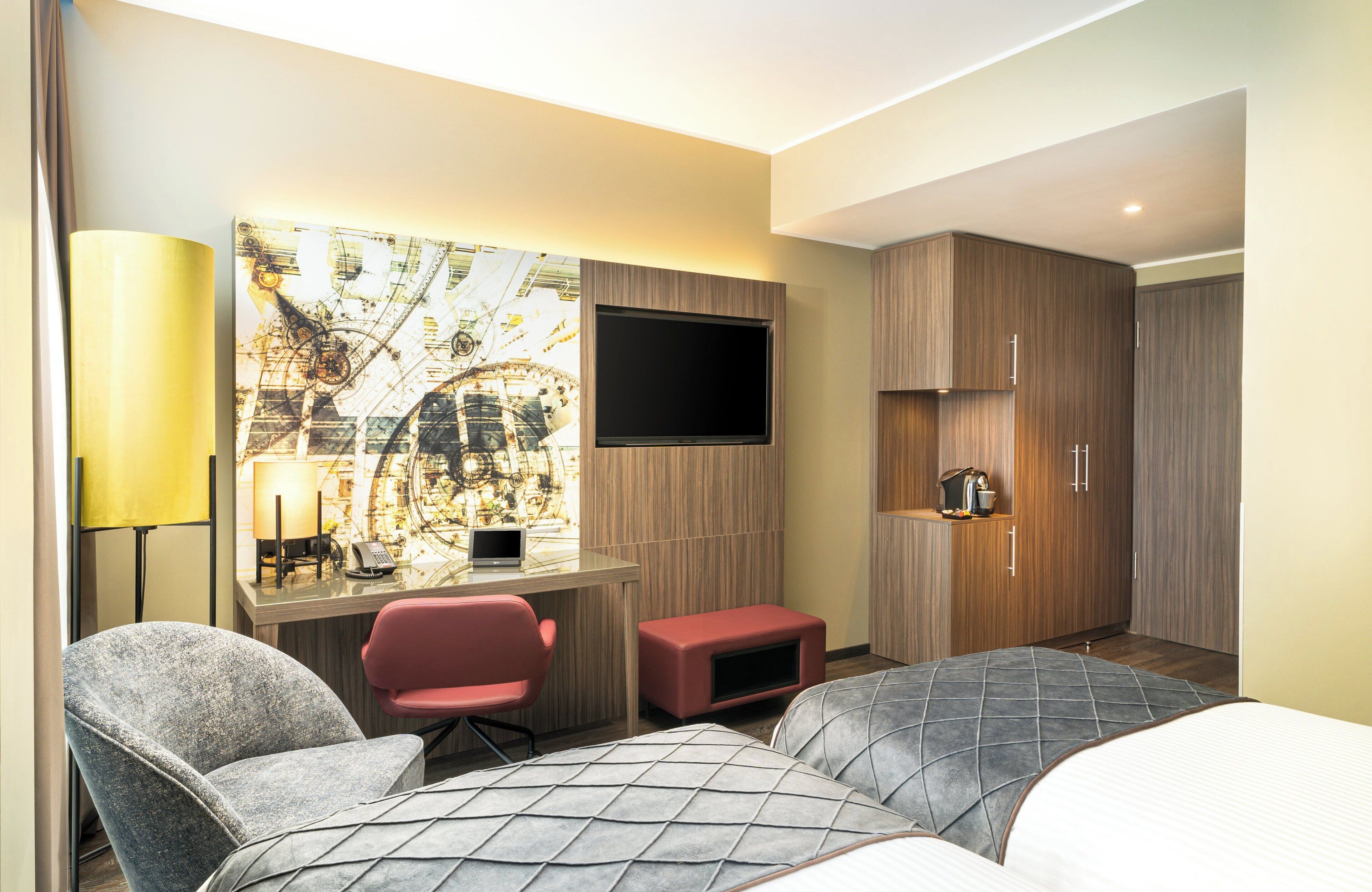 A hotel room with a bed, a desk with a computer, a TV, and a seating area with chairs.