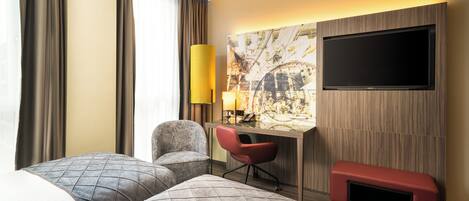 Habitación de hotel con dos camas, un escritorio, una silla, un televisor y un banco rojo.