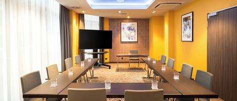 A conference room with a long table, chairs, a flat-screen TV, and artwork on the walls.