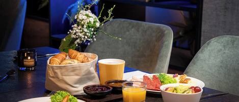 A breakfast setting with croissants, a fruit bowl, and a glass of orange juice on a table.