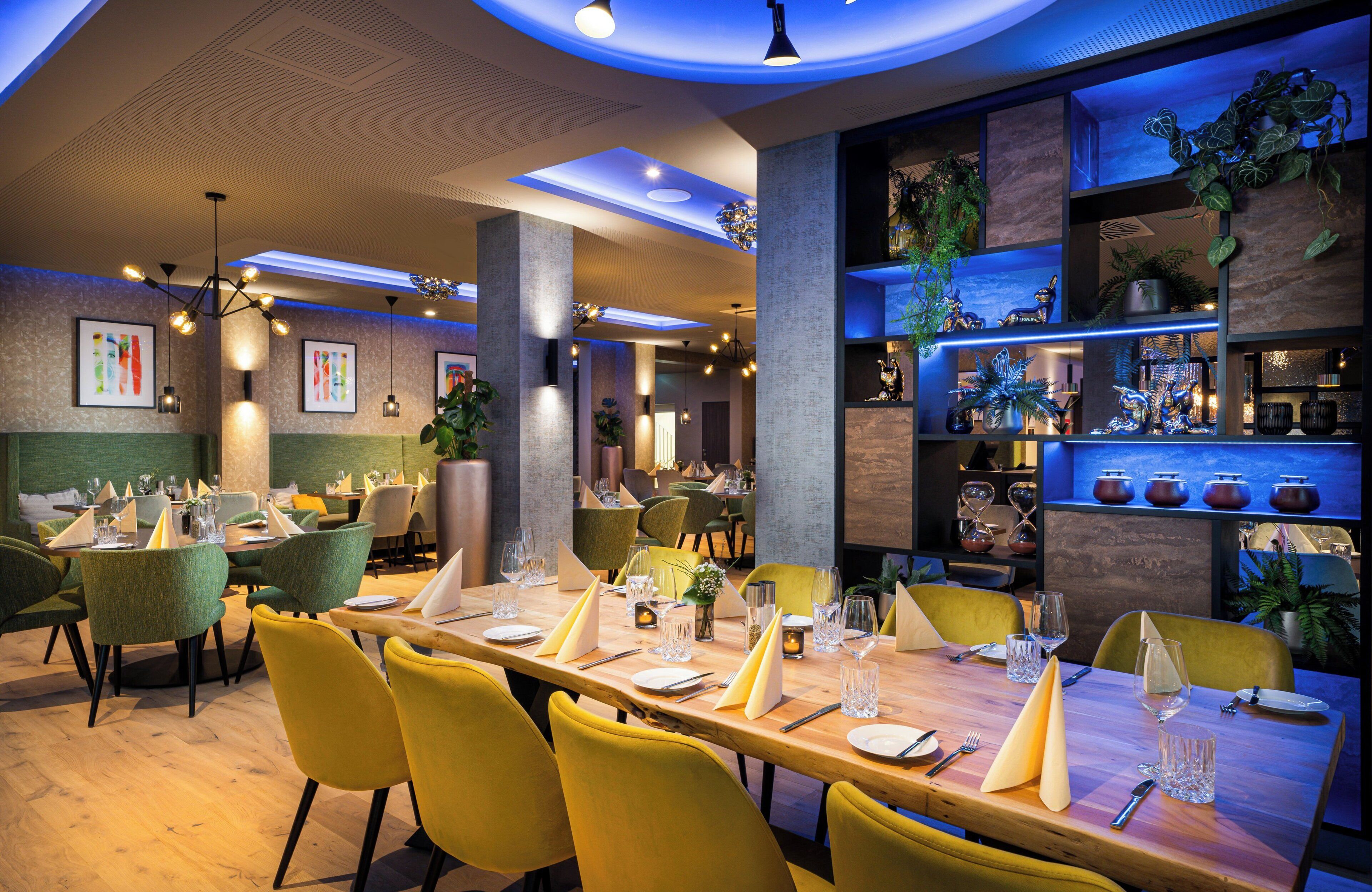 A restaurant with a long wooden table set for dining, surrounded by yellow chairs.