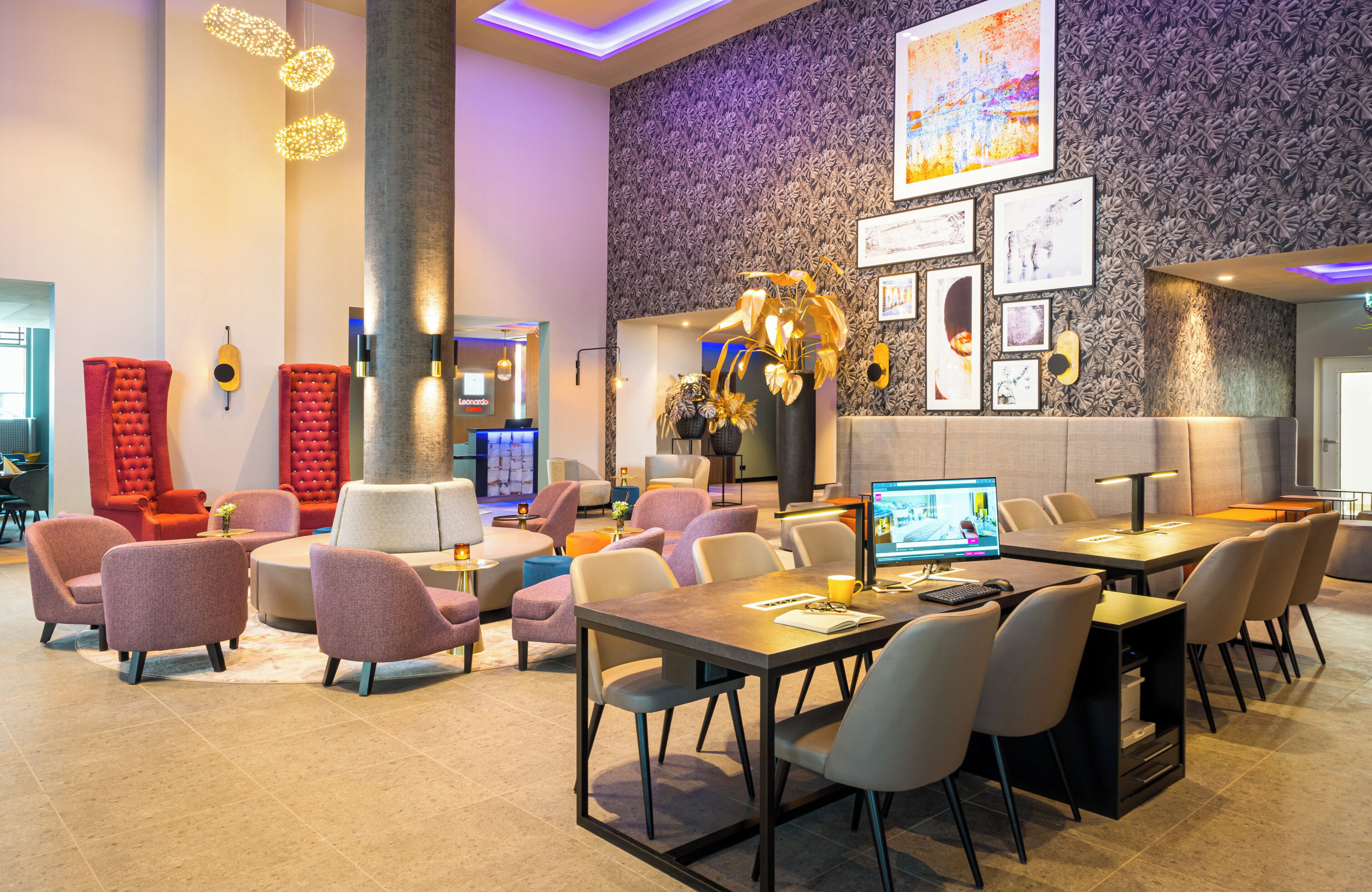 A modern hotel lobby with a mix of seating areas, including round tables and sofas, a large pillar, and a wall adorned with framed pictures and a large abstract painting.