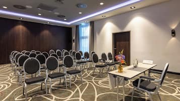 Ein Konferenzraum mit Reihen von Stühlen, einem Tisch und einer Blumenvase sowie einer Tür im Hintergrund.