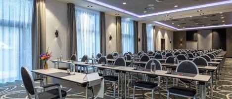 Un salón de conferencias con filas de mesas y sillas, equipado con micrófonos y botellas de agua.