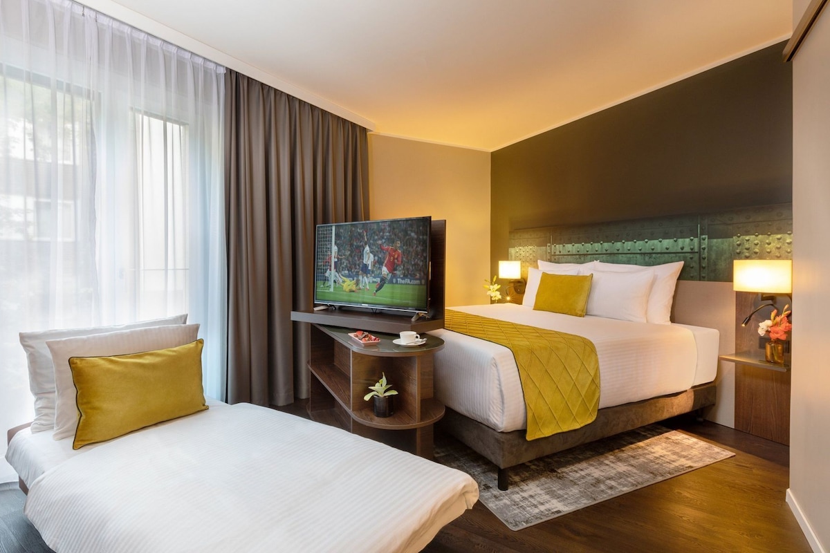 Una habitación de hotel con una cama, un televisor, una mesita de noche con lámpara y una silla.
