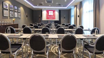 A conference room with tables and chairs, a projector screen displaying the logo of Leonardo Hotels, and framed pictures on the wall.