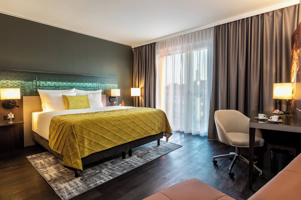 A hotel room with a bed, a desk, a chair, and a large window with curtains.