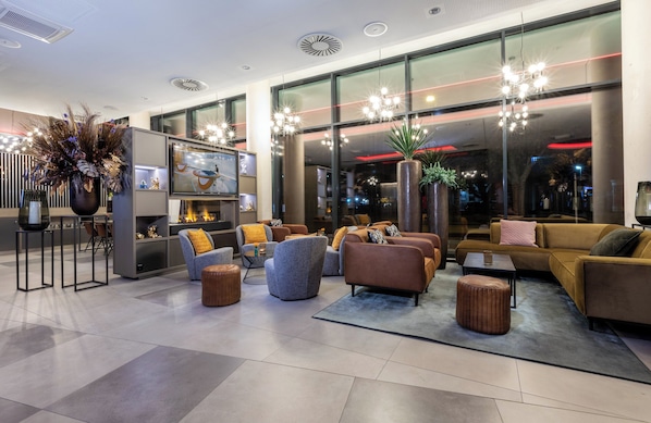 Un lobby moderno con un televisor grande, asientos cómodos y ventanas amplias.