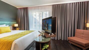 Una habitación de hotel con cama, televisor, una mesita con vasos, sofá y cortinas.