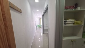 Un couloir avec une porte en bois, une armoire blanche dotée de plusieurs étagères et un sol carrelé.