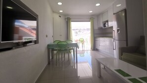 Une cuisine moderne avec un coin repas, un téléviseur à écran plat fixé au mur et une vue sur l’extérieur.