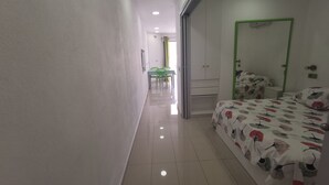 Une chambre d’hôtel avec un lit, une porte verte et un couloir menant à un espace repas équipé de chaises et d’une table.