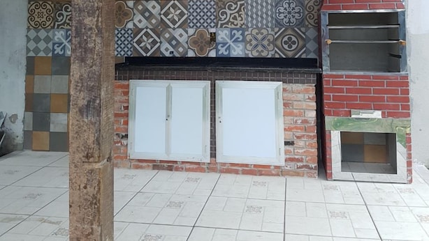 Una cocina al aire libre con protector salpicadero de azulejos, una chimenea de ladrillo y un techo de metal.