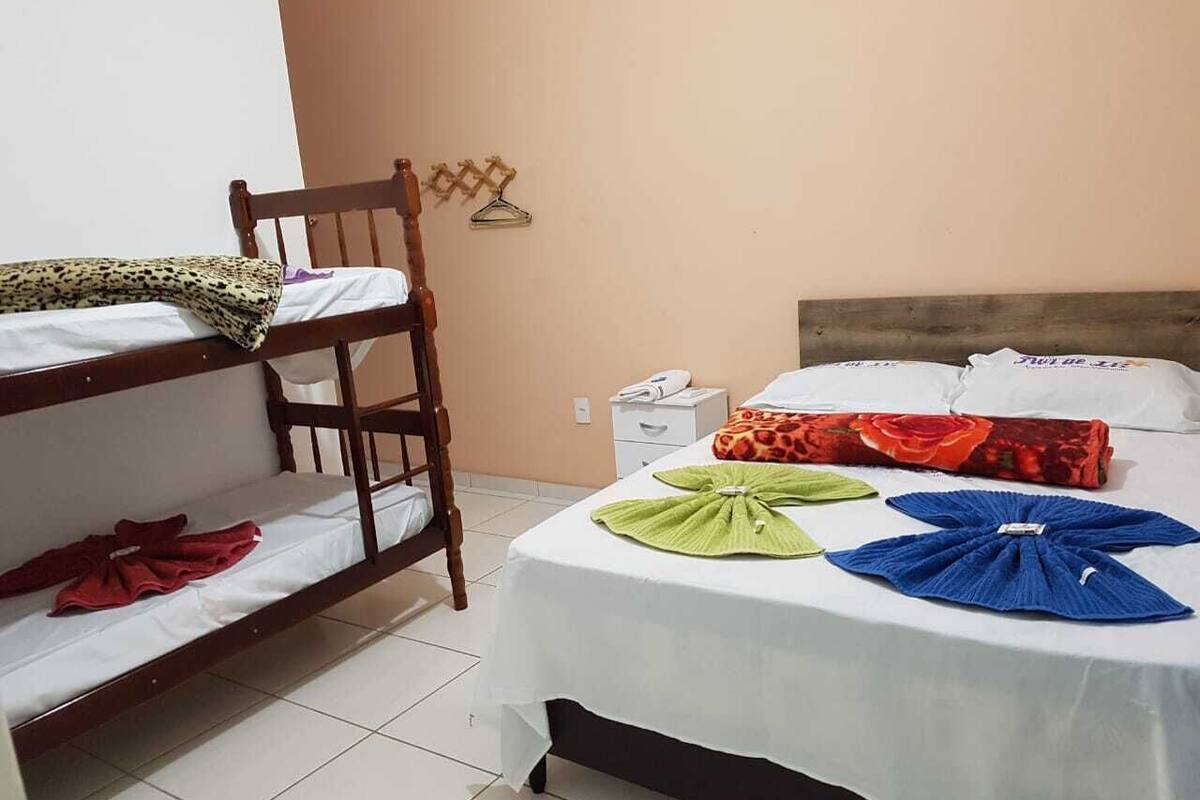 Une chambre avec des lits superposés, un lit simple avec un drap blanc et une petite table de chevet avec une lampe.