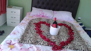 Una cama con un arreglo de pétalos de rosa en forma de corazón y una botella de vino.