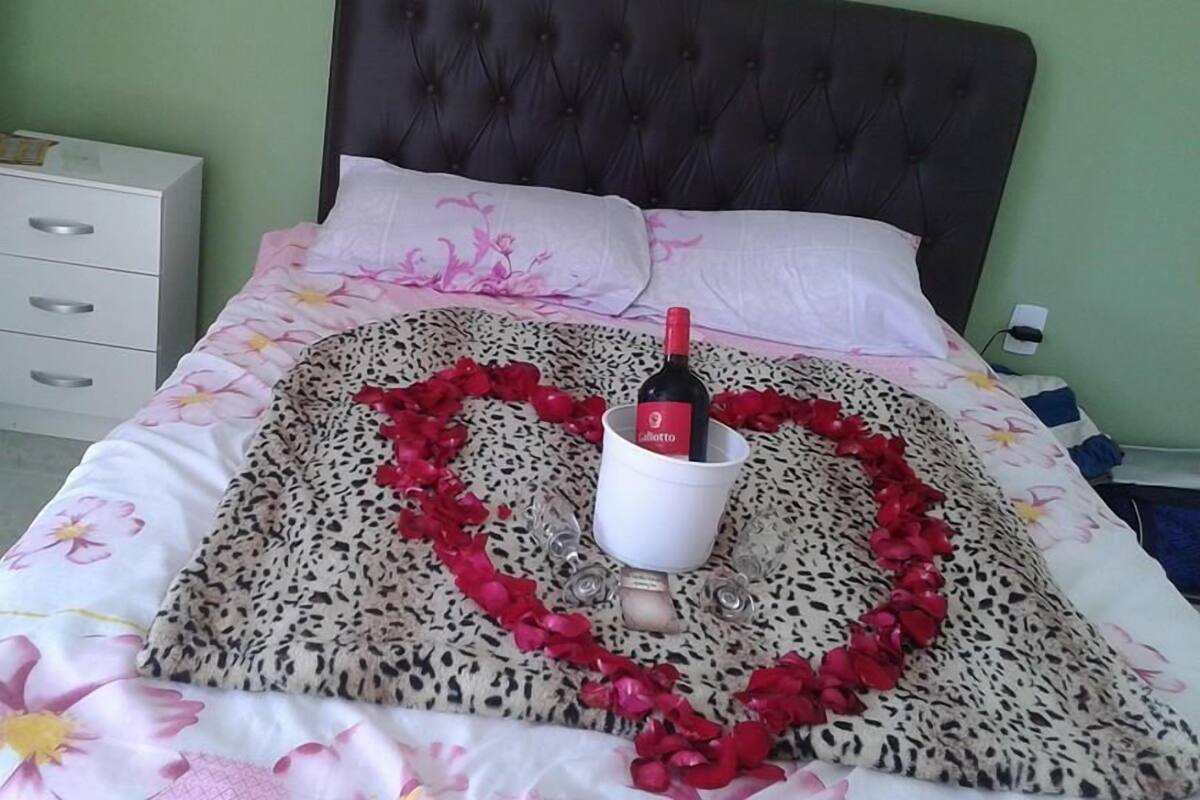 Un lit décoré de pétales de roses disposés en forme de cœur et une bouteille de vin.