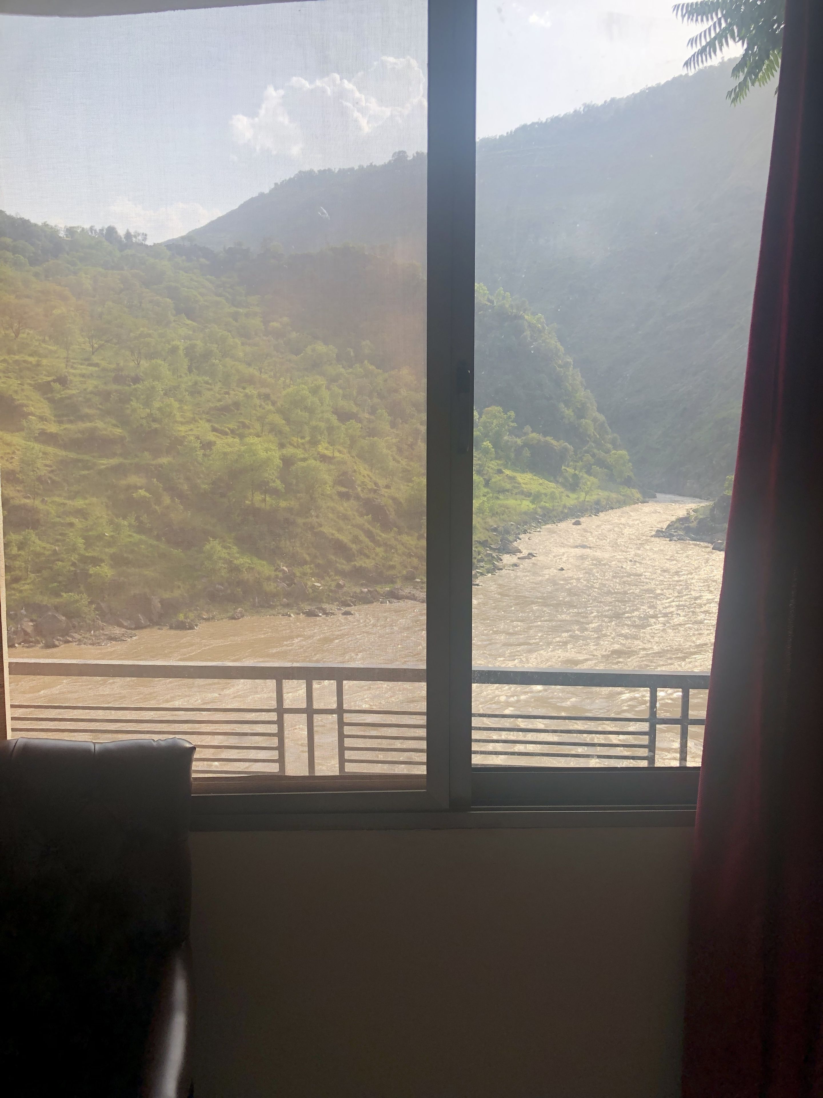Quarto com grande janela com vista para um rio e colinas.
